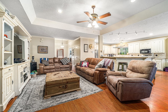 living room with ceiling fan, light hardwood / wood-style floors, a textured ceiling, a tray ceiling, and ornamental molding