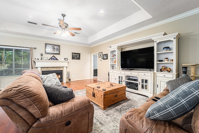 living room featuring a tray ceiling, ceiling fan, ornamental molding, and light hardwood / wood-style floors