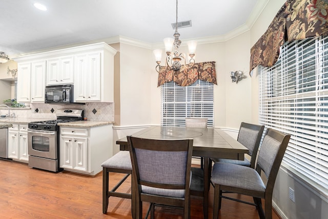 dining room with light hardwood / wood-style floors, crown molding, and an inviting chandelier