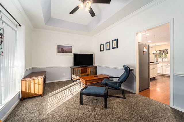 living room featuring hardwood / wood-style flooring, ceiling fan with notable chandelier, a raised ceiling, and crown molding