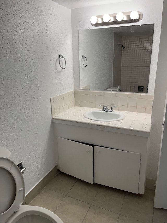 bathroom with vanity, a tile shower, toilet, and tile patterned floors