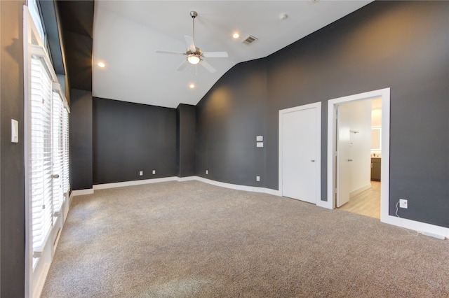 empty room with ceiling fan, high vaulted ceiling, a wealth of natural light, and light colored carpet