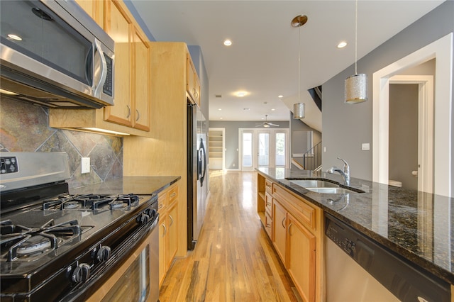 kitchen with stainless steel appliances, dark stone counters, sink, decorative light fixtures, and light hardwood / wood-style floors