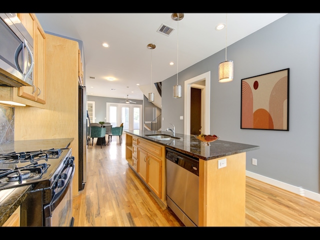 kitchen with a center island with sink, sink, pendant lighting, light hardwood / wood-style floors, and stainless steel appliances