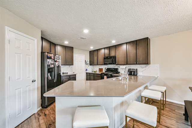 kitchen featuring light hardwood / wood-style flooring, a breakfast bar, black appliances, and kitchen peninsula