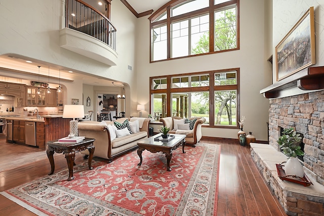 living room featuring a high ceiling, a stone fireplace, crown molding, and dark hardwood / wood-style flooring