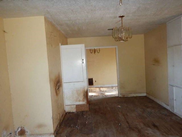 spare room featuring a notable chandelier, a textured ceiling, and dark hardwood / wood-style floors