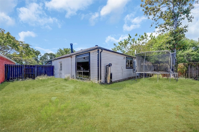 back of house featuring a trampoline and a lawn