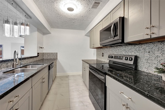 kitchen featuring stainless steel appliances, dark stone counters, sink, a textured ceiling, and tasteful backsplash