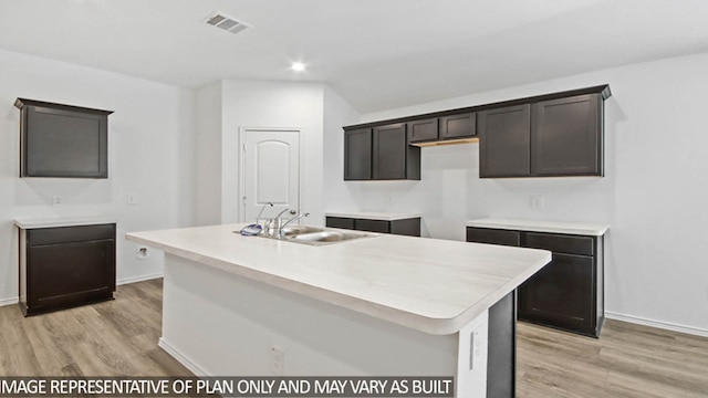 kitchen featuring a center island with sink, sink, dark brown cabinets, and light wood-type flooring