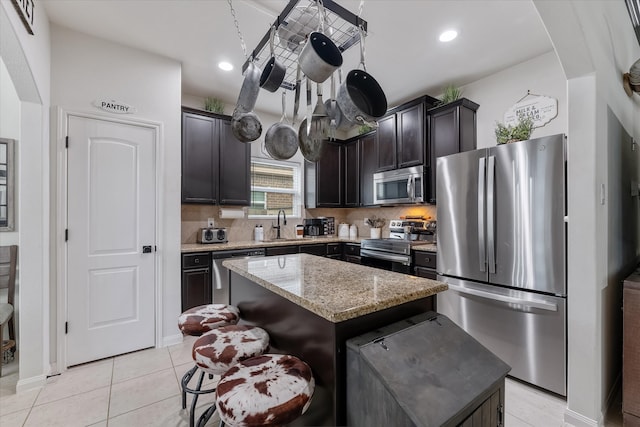 kitchen featuring stainless steel appliances, sink, a center island, dark brown cabinetry, and light stone counters