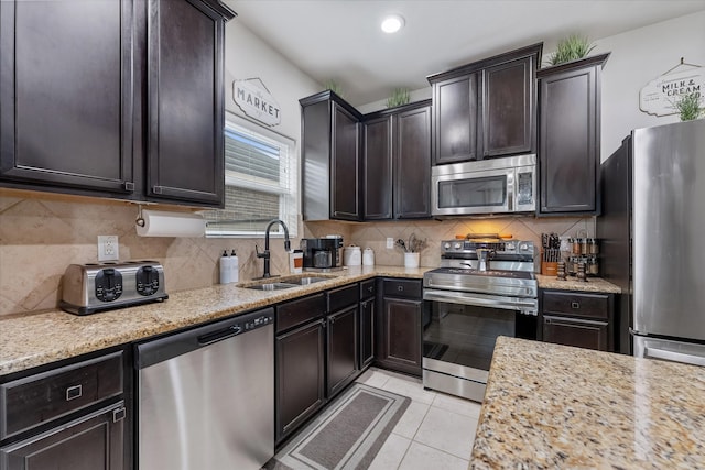 kitchen featuring dark brown cabinets, appliances with stainless steel finishes, light stone countertops, light tile patterned flooring, and sink