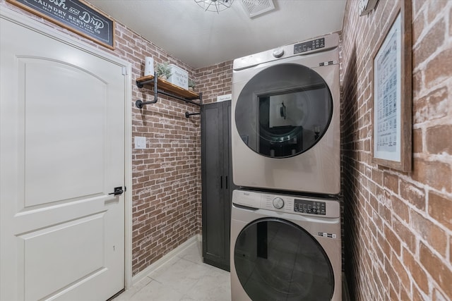 laundry area featuring stacked washer and dryer and brick wall