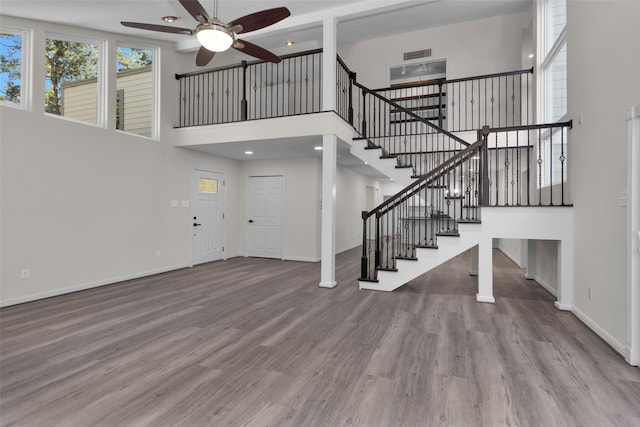 unfurnished living room featuring wood-type flooring, ceiling fan, and a towering ceiling