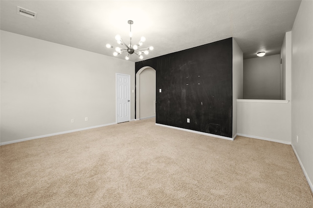 spare room featuring light colored carpet and a notable chandelier