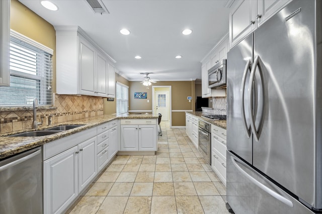 kitchen with appliances with stainless steel finishes, sink, kitchen peninsula, white cabinets, and decorative backsplash