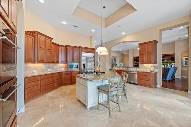 kitchen with tasteful backsplash, hanging light fixtures, a breakfast bar area, an island with sink, and built in appliances