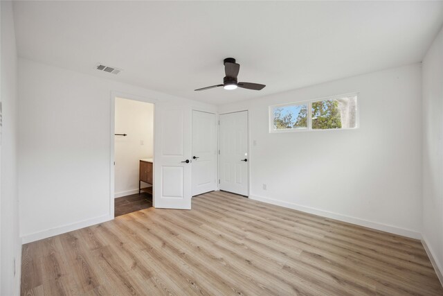 unfurnished bedroom featuring ensuite bath, light wood-type flooring, and ceiling fan