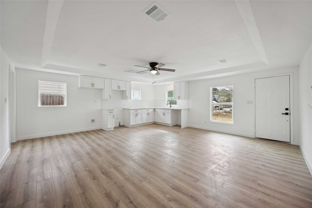 unfurnished living room with light hardwood / wood-style floors, a raised ceiling, sink, and ceiling fan