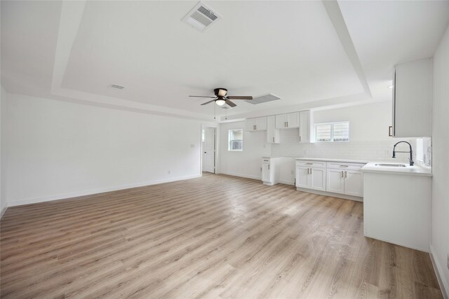 unfurnished living room with sink, a raised ceiling, light wood-type flooring, and ceiling fan