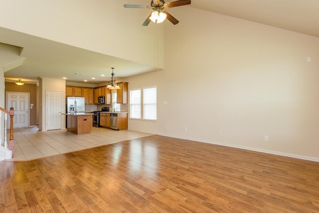 unfurnished living room featuring light hardwood / wood-style floors, high vaulted ceiling, and ceiling fan with notable chandelier