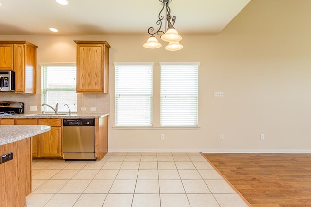 kitchen featuring tasteful backsplash, an inviting chandelier, light stone countertops, stainless steel appliances, and decorative light fixtures