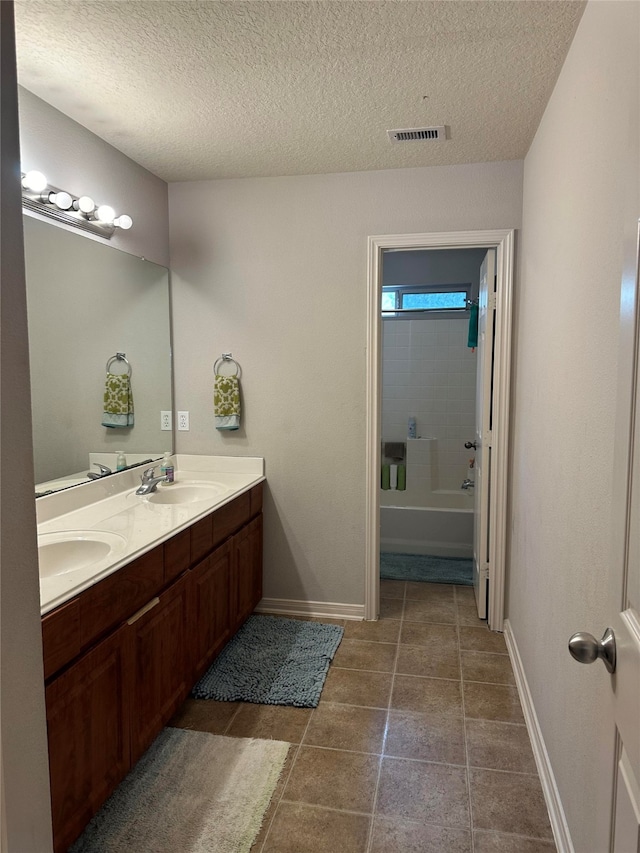 bathroom with tile patterned flooring, vanity, a textured ceiling, and tiled shower / bath