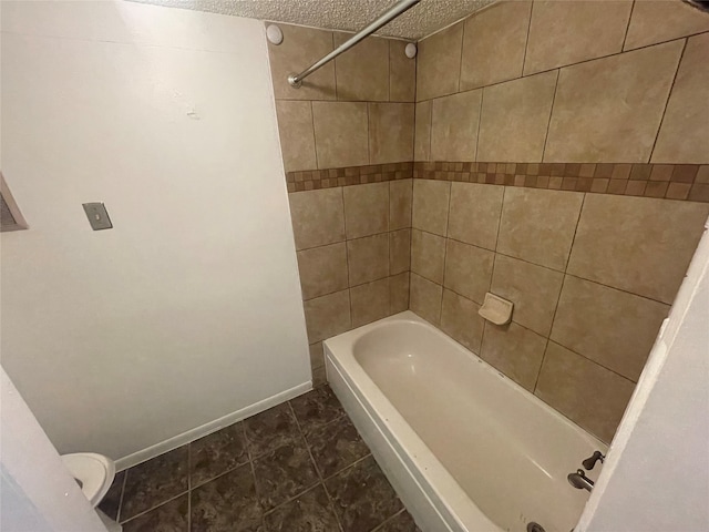 bathroom featuring tiled shower / bath, tile patterned floors, a textured ceiling, and toilet