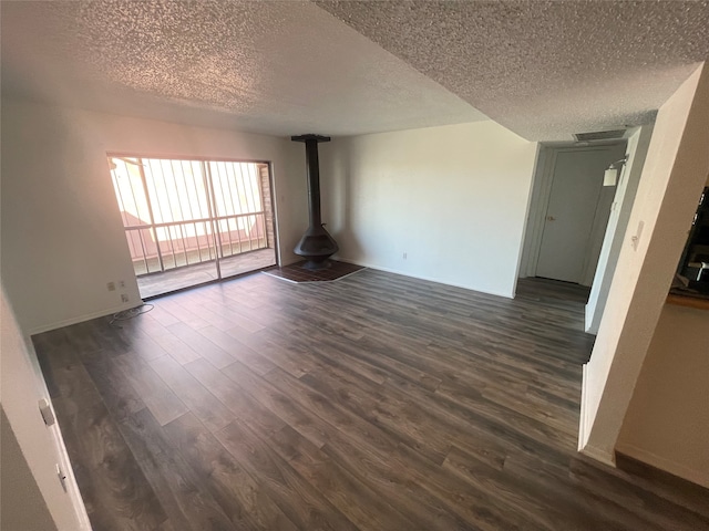 spare room featuring dark wood-type flooring, a textured ceiling, and a wood stove