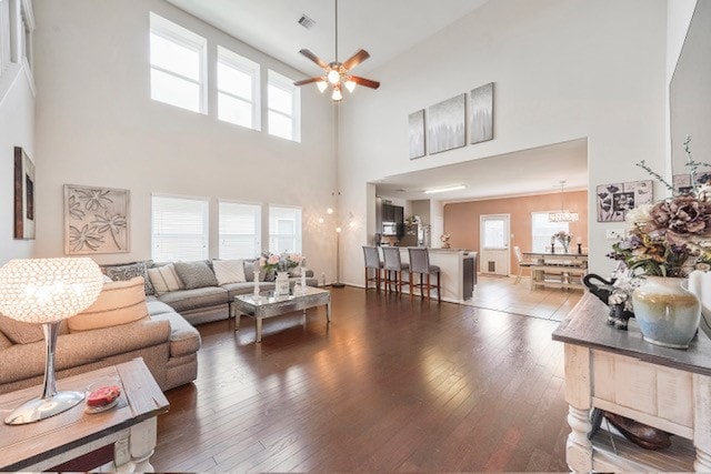 living room with a towering ceiling, a healthy amount of sunlight, hardwood / wood-style flooring, and ceiling fan with notable chandelier