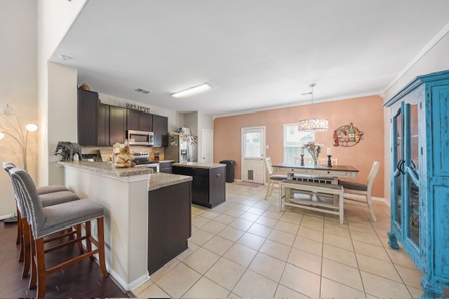 kitchen featuring hanging light fixtures, kitchen peninsula, stainless steel appliances, light stone countertops, and light tile patterned flooring