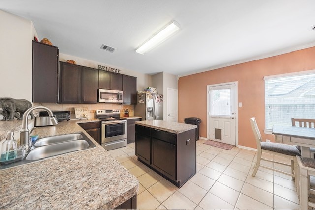 kitchen with a kitchen island, dark brown cabinets, stainless steel appliances, sink, and light tile patterned flooring