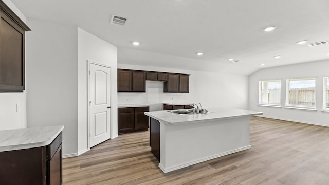 kitchen featuring vaulted ceiling, dark brown cabinetry, a kitchen island with sink, and light hardwood / wood-style flooring