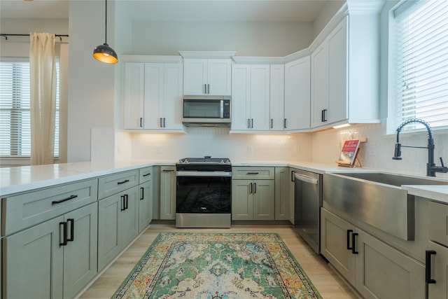 kitchen with tasteful backsplash, appliances with stainless steel finishes, pendant lighting, sink, and light hardwood / wood-style floors