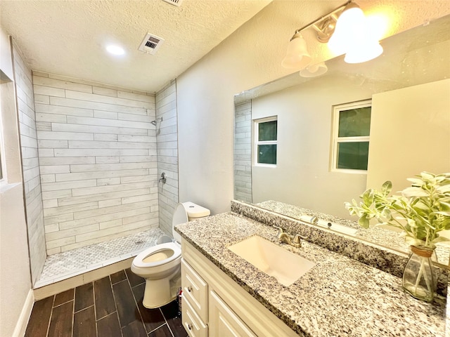 bathroom featuring vanity, toilet, a textured ceiling, and a tile shower