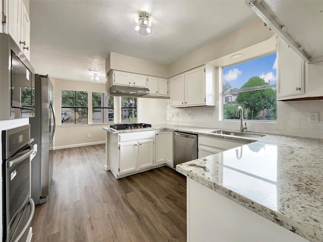 kitchen featuring stainless steel appliances, white cabinets, kitchen peninsula, decorative backsplash, and light stone countertops