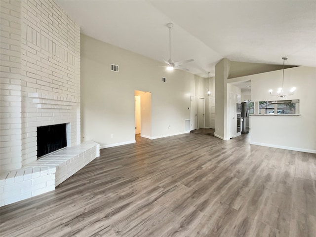 unfurnished living room with high vaulted ceiling, hardwood / wood-style floors, ceiling fan with notable chandelier, and a brick fireplace