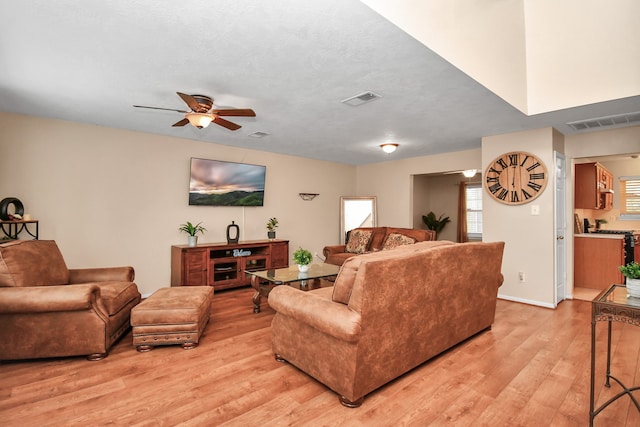 living room with ceiling fan, a textured ceiling, and light wood-type flooring