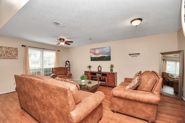 living room featuring ceiling fan, light hardwood / wood-style flooring, and a textured ceiling