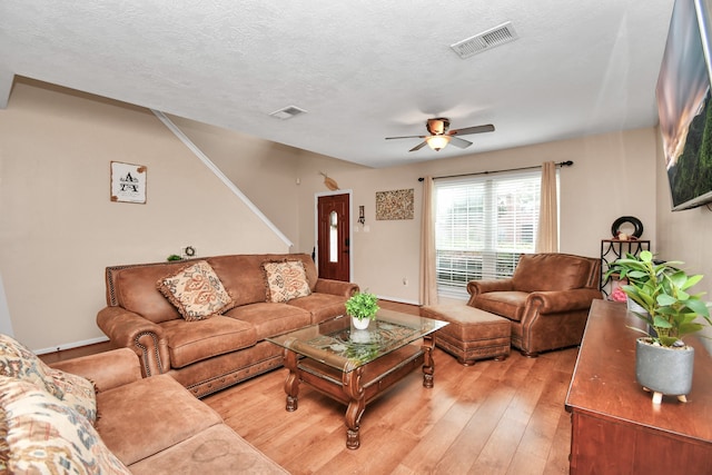 living room with ceiling fan, light wood-type flooring, and a textured ceiling