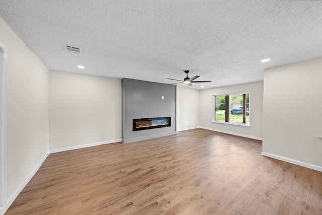 unfurnished living room with a large fireplace, a textured ceiling, light wood-type flooring, and ceiling fan