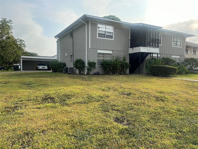 view of side of home with a yard, central air condition unit, a carport, brick siding, and board and batten siding