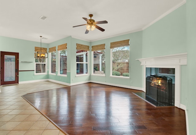 unfurnished living room with crown molding, ceiling fan with notable chandelier, light wood-type flooring, and a wealth of natural light