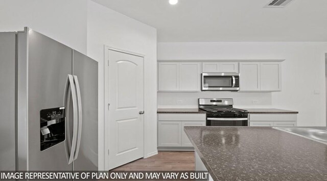 kitchen with appliances with stainless steel finishes, white cabinetry, dark stone countertops, sink, and light hardwood / wood-style flooring