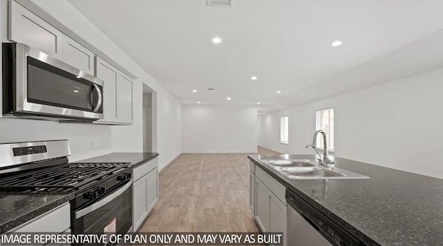 kitchen with sink, stainless steel appliances, dark stone counters, and light wood-type flooring