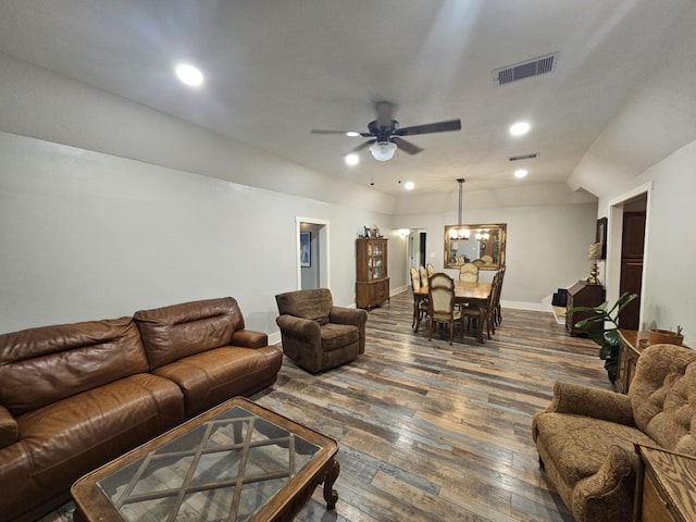 living room featuring ceiling fan with notable chandelier, dark wood-type flooring, and vaulted ceiling