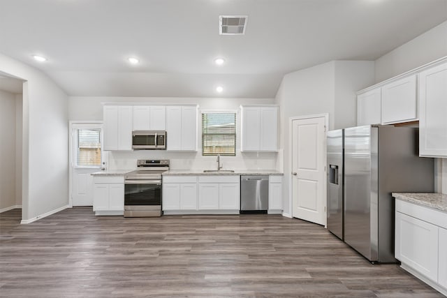 kitchen featuring sink, vaulted ceiling, white cabinetry, light wood-type flooring, and appliances with stainless steel finishes