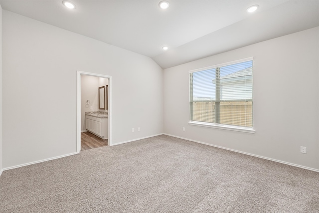 unfurnished bedroom featuring lofted ceiling, light carpet, and ensuite bath