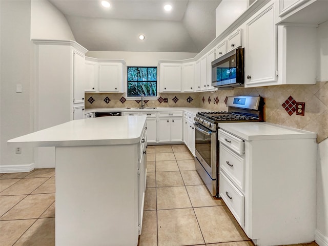 kitchen featuring appliances with stainless steel finishes, sink, vaulted ceiling, white cabinets, and a center island