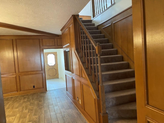 staircase with hardwood / wood-style floors, lofted ceiling, and a textured ceiling